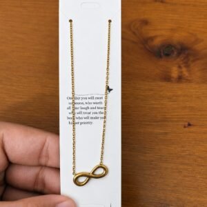 Gold-tone infinity pendant necklace displayed on a stainless steel card