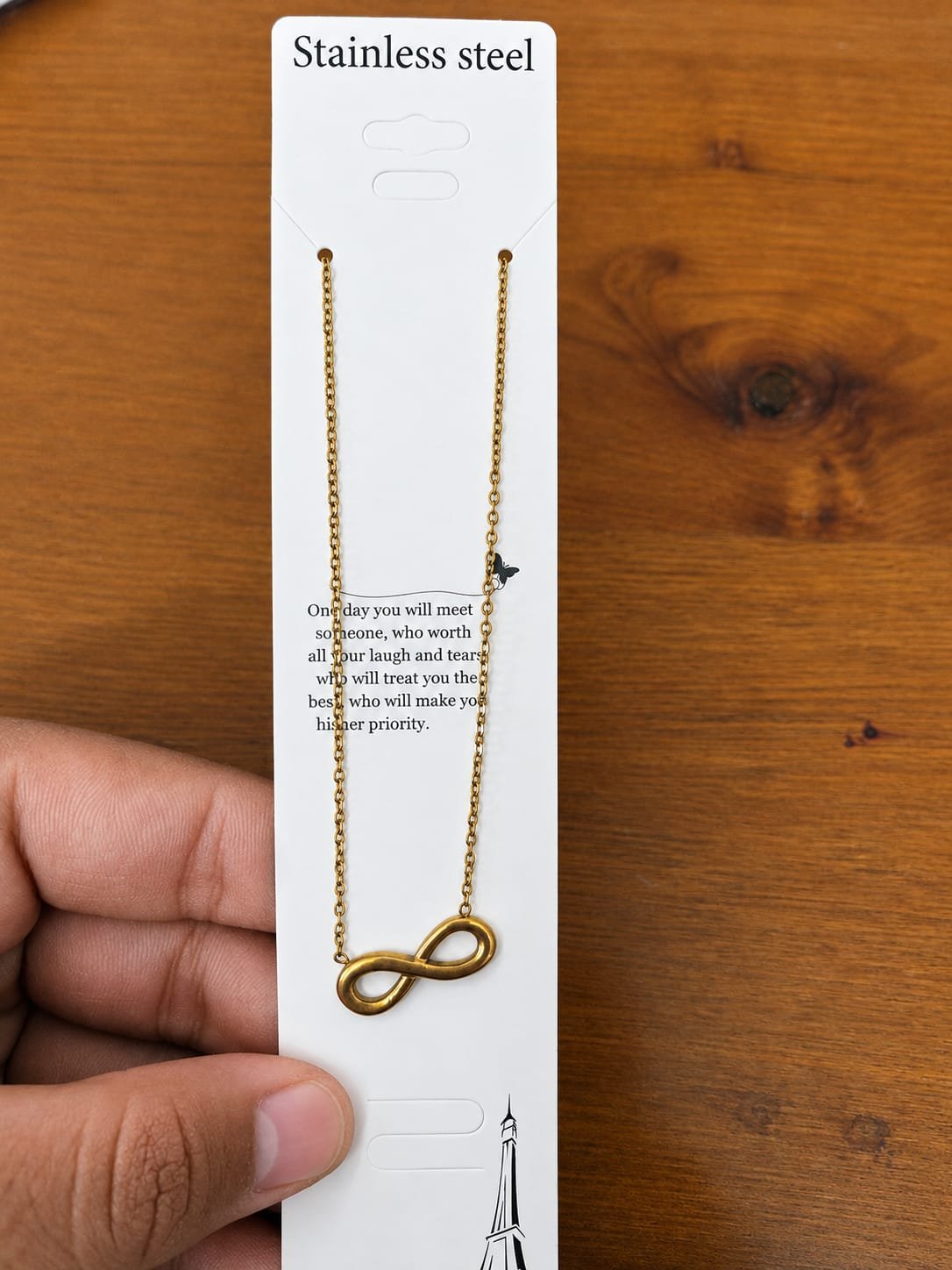 Gold-tone infinity pendant necklace displayed on a stainless steel card